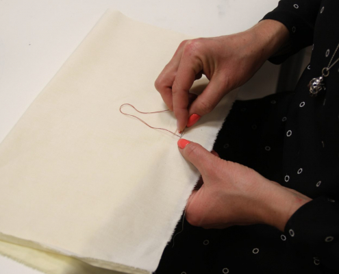 Frau näht mit der Hand an einem Stoffstück