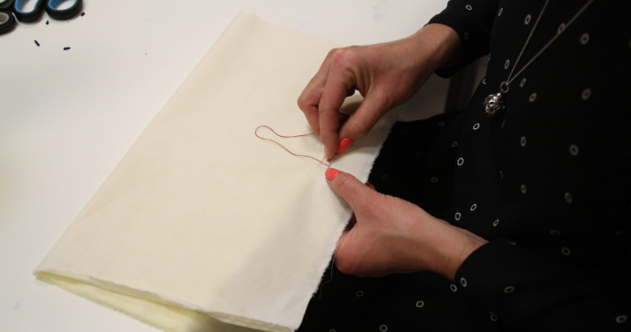 Frau näht mit der Hand an einem Stoffstück